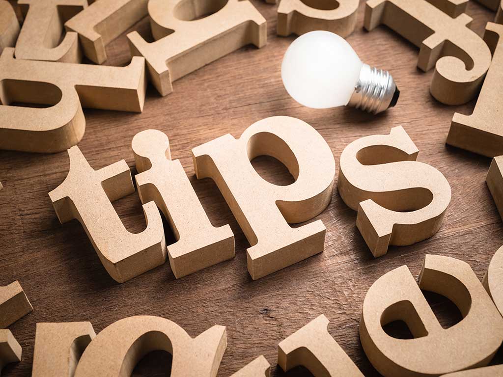 Scattered wooden letters on a wood surface with four of the letters spelling out the word tips with a lightbulb above it